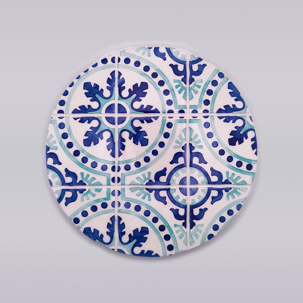 A circular mosaic tile design featuring intricate blue and teal patterns. The design includes symmetrical floral and geometric shapes, with a central star-like motif surrounded by leafy elements, bordered by dots and curved lines. This Chaves Ceramic Tile Trivet from Tejo Shop offers both artistic beauty and heat protection for your kitchen.
