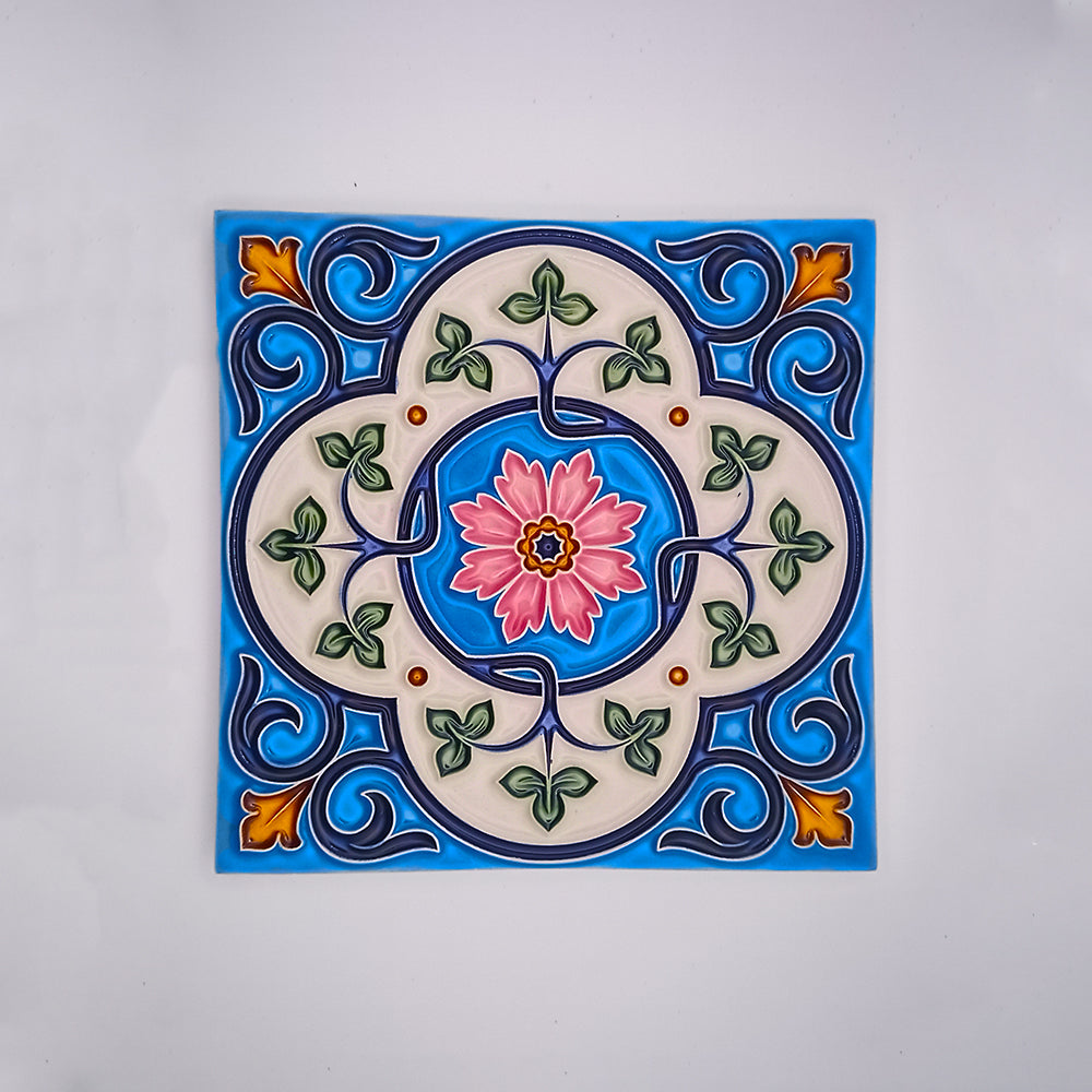 A colorful hand-painted Tejo Shop ceramic tile featuring a symmetrical design with a pink flower at the center, surrounded by blue and green floral patterns, set against a white background.