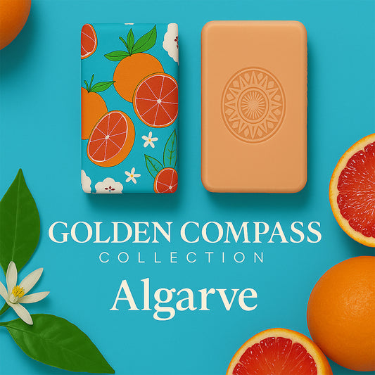 Two soap bars—one with an orange fruit pattern, one plain with a sun design—rest on a blue background with sliced oranges, green leaves, and white flowers. Text: "100ml Algarve 1434 – Edge of the Known World handcrafted soap.