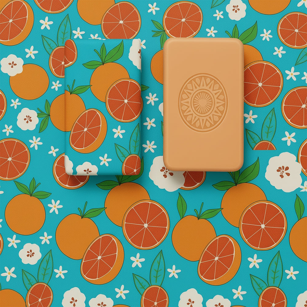 The Algarve 1434 – Edge of the Known World soap by 100ml and its box rest on a blue surface with an orange and white citrus floral pattern, featuring oranges and blossoms. Handcrafted in Portugal.