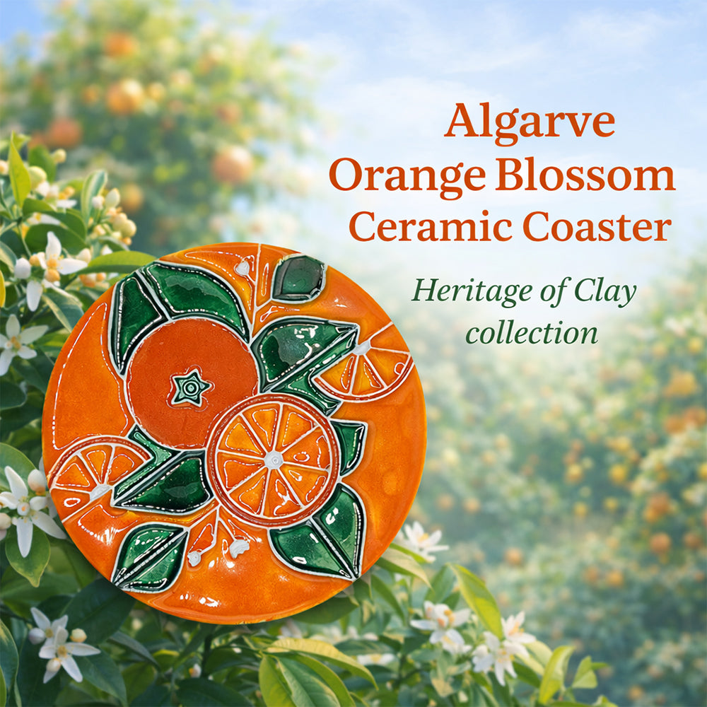 A vibrant ceramic coaster from Miradouro Ceramics, featuring orange and green designs of oranges and leaves, is shown on an orange blossom background. Text: "Algarve Orange Blossom Ceramic Coaster. Heritage of Clay collection.
