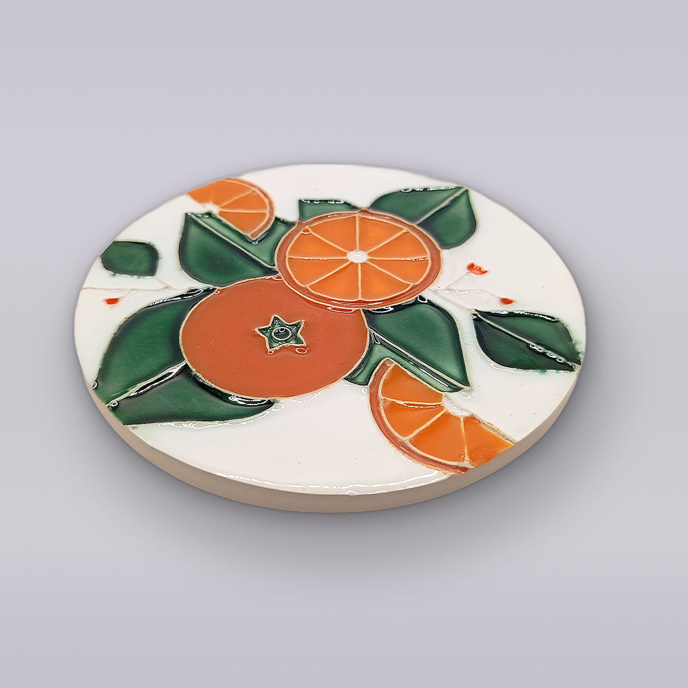 Miradouro Ceramics’ Algarve Orange Harvest Ceramic Coaster features a hand-painted design of oranges, orange slices, and green leaves on a white background.
