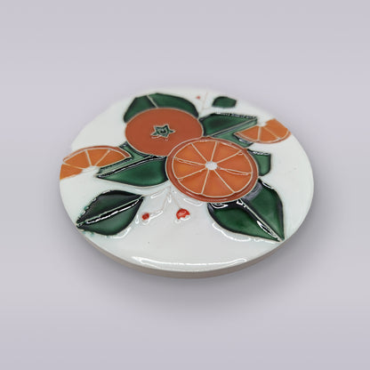 The Algarve Orange Harvest Ceramic Coaster by Miradouro Ceramics features an embossed design of oranges, slices, and green leaves on a crisp white background.