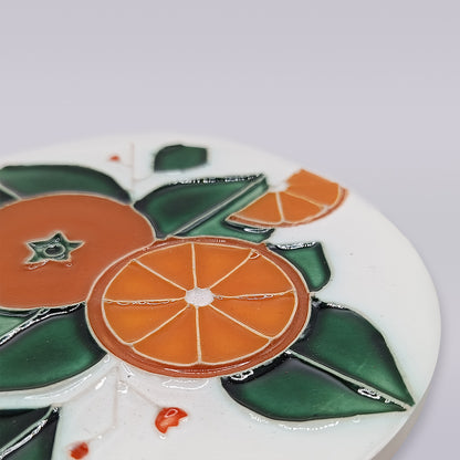 A close-up of the Miradouro Ceramics Algarve Orange Harvest Ceramic Coaster, displaying an orange fruit and slice with green leaves, all outlined in black on a white background.