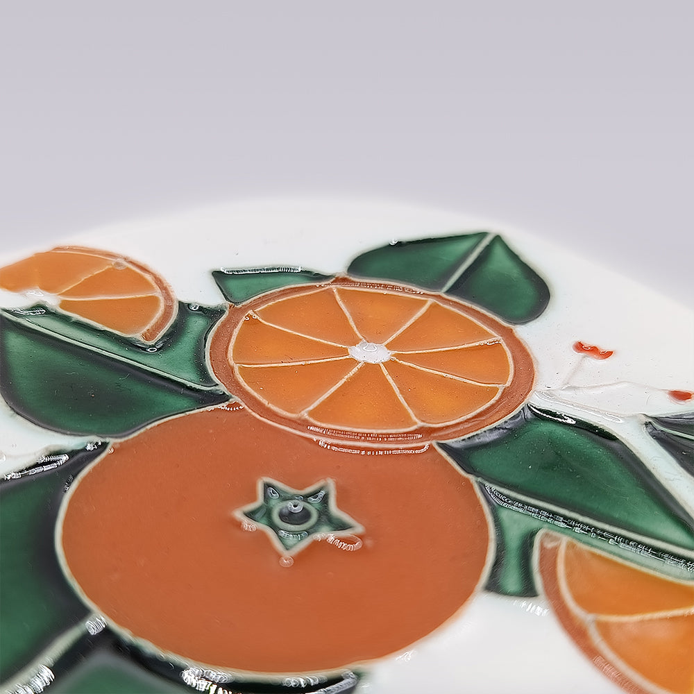 Close-up of the Miradouro Ceramics Algarve Orange Harvest Ceramic Coaster, handmade and hand-painted with orange slices and green leaves on a white background, inspired by Portugal's Algarve harvest.