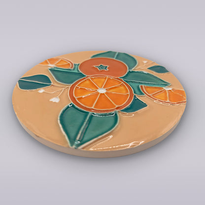 The Miradouro Ceramics Algarve Sandstone Orange Ceramic Coaster features an embossed pattern of orange slices and green leaves on a beige background.