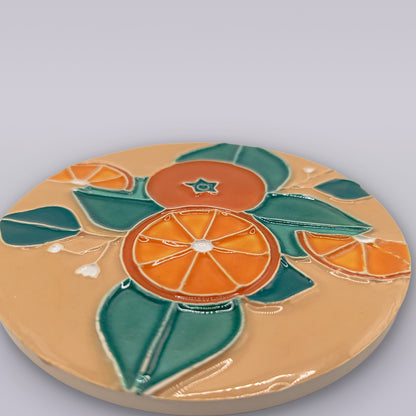 The Miradouro Ceramics Algarve Sandstone Orange Ceramic Coaster features embossed orange citrus slices and green leaves on a beige background, finished with a glossy sheen.