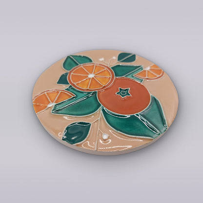 The Algarve Sandstone Orange Ceramic Coaster by Miradouro Ceramics features embossed colorful oranges and green leaves on light beige—adding charming Portuguese style to any table setting.