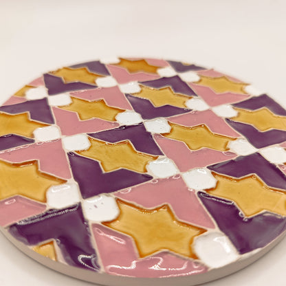 The Azulejo Pop coaster by Miradouro Ceramics is a round handmade ceramic tile with glossy finish, featuring a geometric pattern of yellow stars on alternating pink, purple, and white backgrounds.