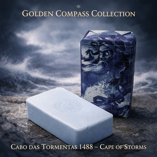 Two rectangular soaps rest on stone: one, wrapped in art of a bearded sailor and stormy sea; the other, unwrapped, pale blue, stamped with a compass. Scented marine accord & sandalwood. 100ml Cabo das Tormentas 1488 – Cape of Storms.