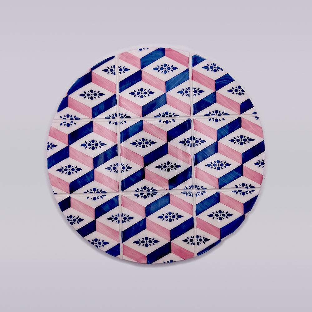 A circular ceramic plate featuring a geometric pattern. The design includes blue and pink hexagons interlocking with each other, and small floral motifs inside some of the hexagons, creating a visually intricate and colorful effect against a white background, perfect as an Evora Ceramic Trivets for Hot Dishes by Tejo Shop.