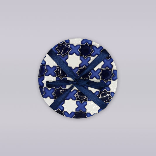 The Évora Star Azulejo Coaster by Miradouro Ceramics features a blue and white geometric design, tied with a dark blue ribbon, set on a light gray background—perfect as handmade home décor.