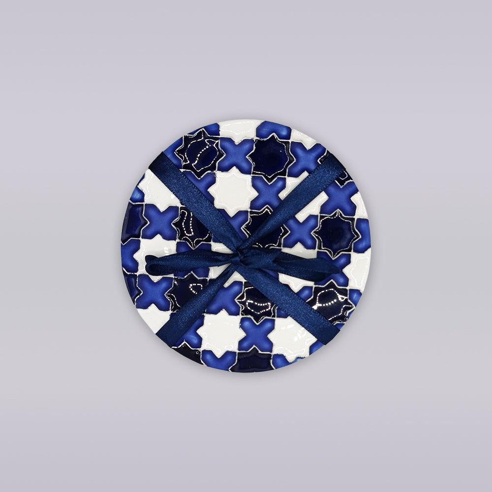 The Évora Star Azulejo Coaster by Miradouro Ceramics features a round Portuguese ceramic design with a blue and white geometric star-cross pattern, wrapped in a dark blue ribbon—ideal as handmade home decor.