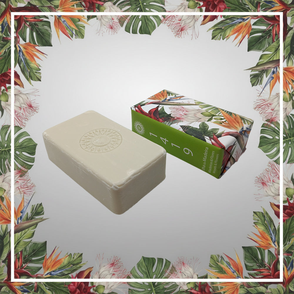 The Ilha da Madeira 1419 – The Atlantic Garden soap by 100ml, a rectangular white bar with Madeira fragrance, is shown beside its floral-patterned box on a background bordered by tropical leaves and flowers.