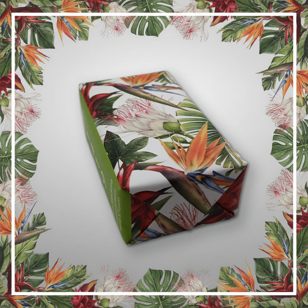 A rectangular gift wrapped in vibrant Ilha da Madeira 1419 – The Atlantic Garden paper by 100ml, featuring green leaves and orange, red, and white flowers, sits on a white background with a matching floral border.