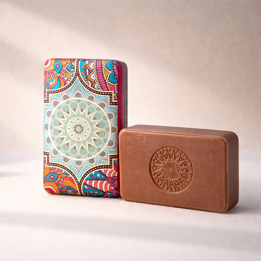 A brown bar of Índia 1498 – Route of Spices soap by 100ml, with a stamped mandala design, stands by its colorful packaging featuring an intricate circular mandala and evokes an Indian-inspired scent on a neutral background.