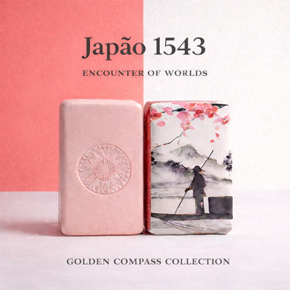 Two decorative soap bars stand upright: one is solid pink with a circular emblem, the other features Japanese-inspired art depicting a figure by water. Text reads: “Japão 1543 – Encounter of Worlds. Golden Compass Collection.” Brand: 100ml.