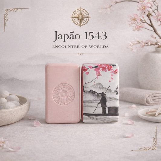Two upright rectangular soap bars: one is pale pink with an embossed design, the other shows a painting of a person on a boat with cherry blossoms and mountains. Text: "Japão 1543 – Encounter of Worlds by 100ml.