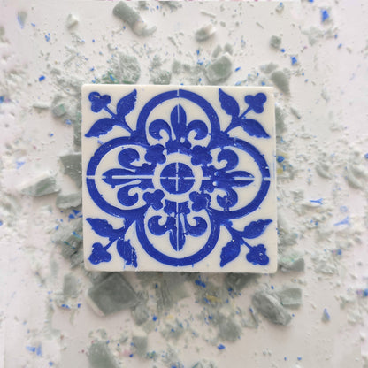 A square ceramic tile with an intricate blue floral and geometric pattern on white, surrounded by light blue and white tile fragments, evokes the charming Lisbão Jasmine Courtyard Soap packaging.