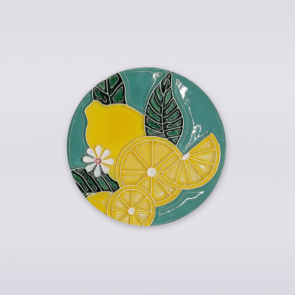 The Lemon Blossom Hand-Painted Ceramic Coaster by Miradouro Ceramics features yellow lemons, slices, green leaves, and white flowers on teal—a stunning piece of Portuguese artisan homeware.