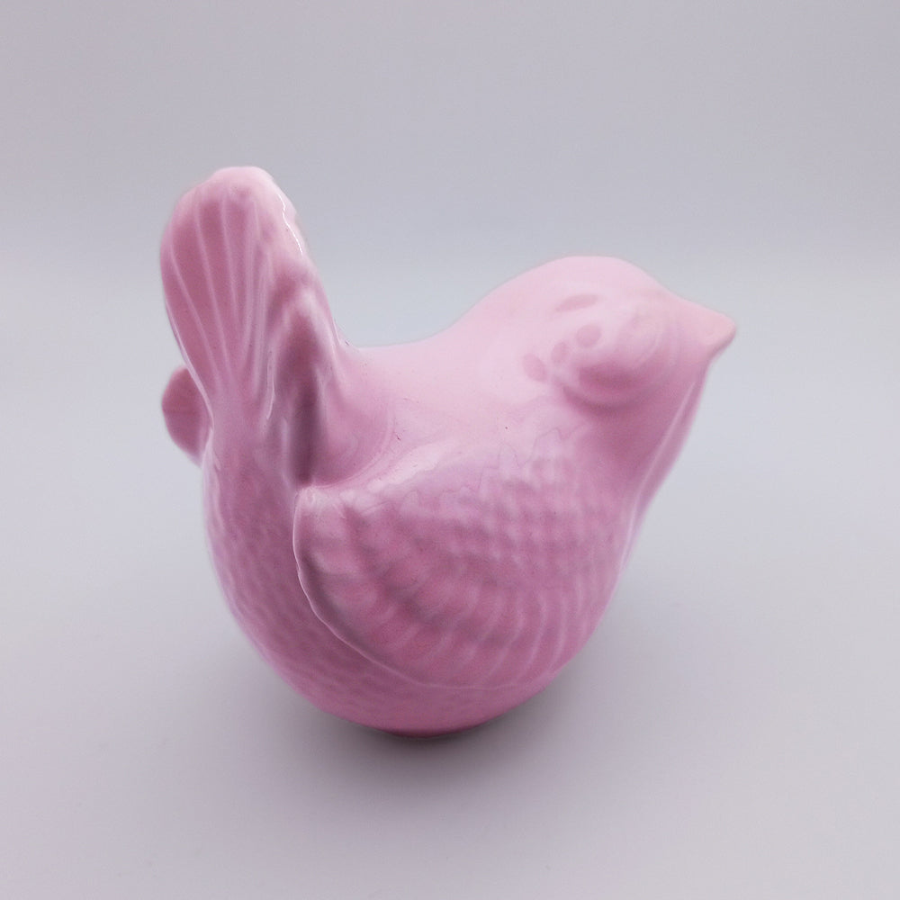 The Ceramic Bird Figurine from Tejo Shop is a small, smooth, glossy pink ceramic sculpture with textured wings and tail. Set against a plain gray background, this rounded and stylized bird offers a decorative and polished look that can enhance any home decor collection with its charm.