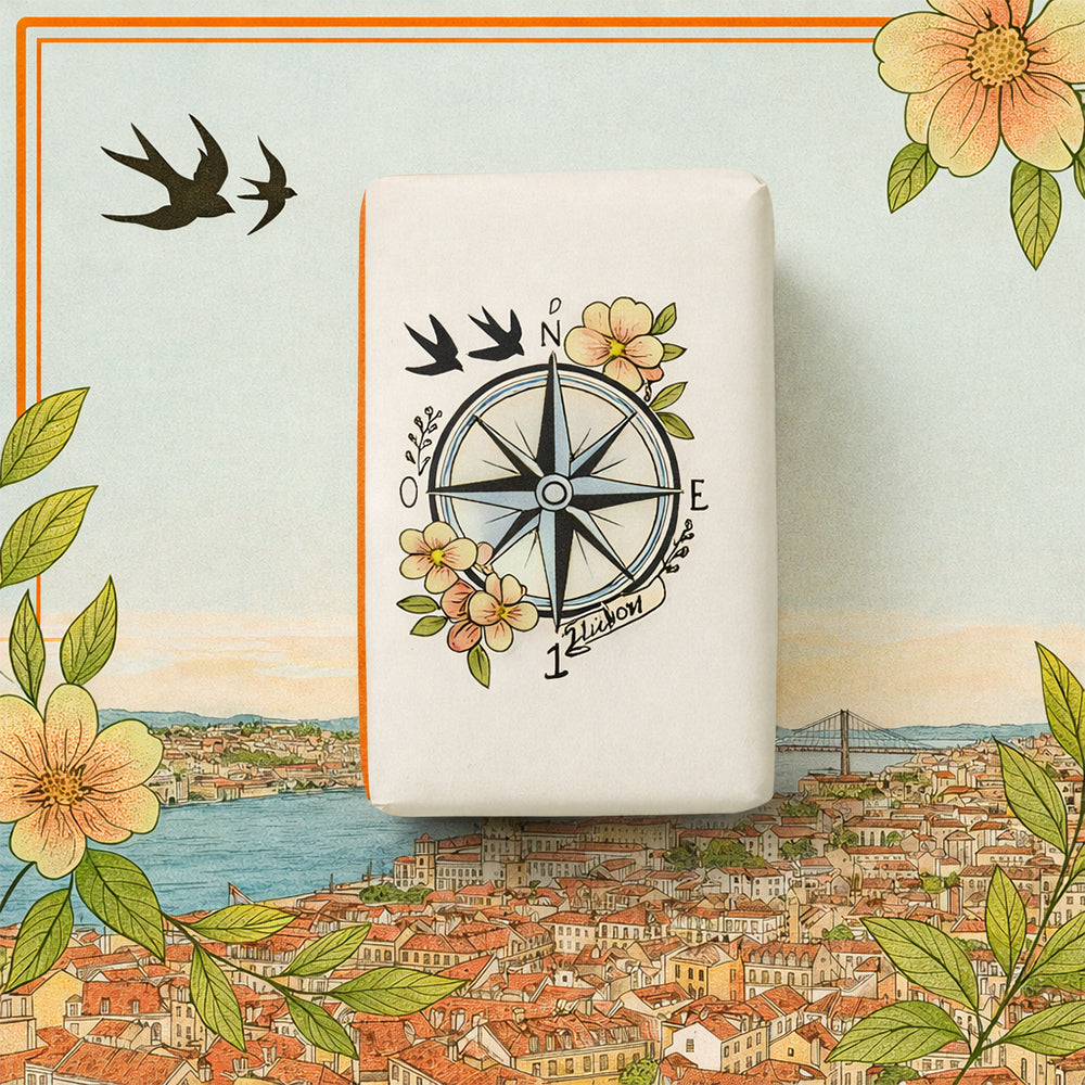 Lisbon 1497 – Gateway to the Oceans by 100ml is a decorated soap, wrapped with a compass, flowers, and birds, displayed on a vibrant map showing a river, flowers, buildings, and a bridge.