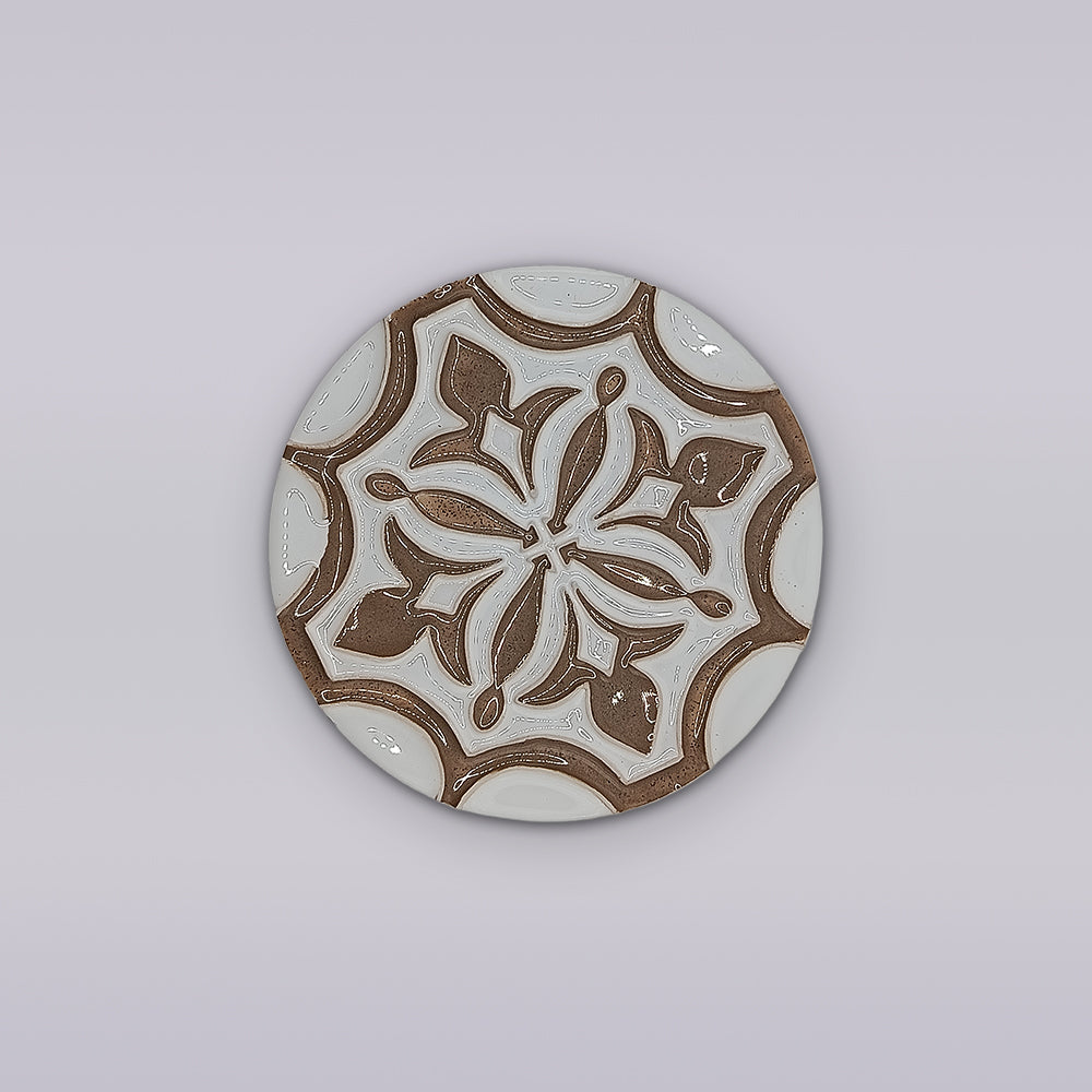 The Lusitana TerraFleur by Miradouro Ceramics is a round ceramic tile featuring intricate brown and white floral and geometric patterns on light gray, inspired by Portuguese handcrafted decorative tile traditions.