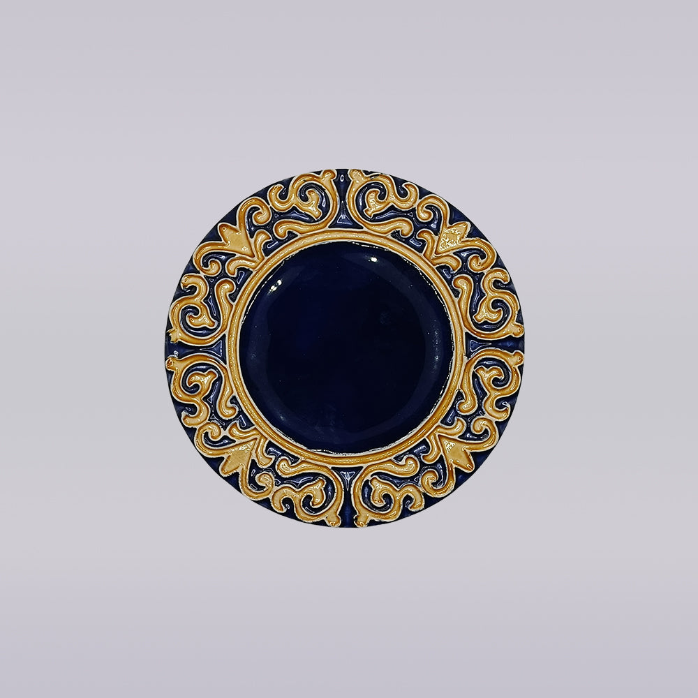 The Manuel I Royal Crest Ceramic Coaster by Miradouro Ceramics features a round shape with a deep blue center and an ornate gold and blue border inspired by Manueline art, set on a light neutral background.