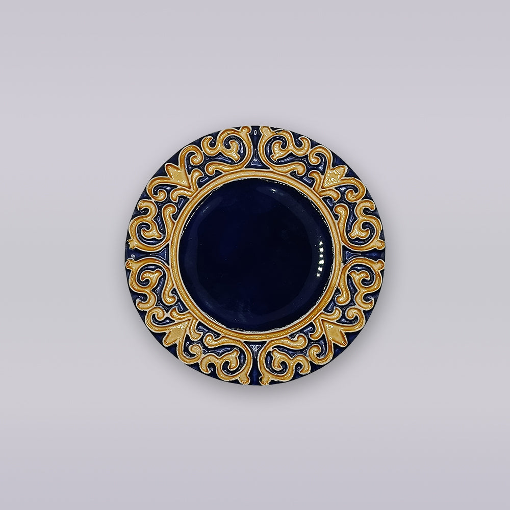 The Manuel I Royal Crest Ceramic Coaster by Miradouro Ceramics is a round, dark blue Portuguese piece with a gold, Manueline-inspired patterned border, shown against a light gray background.