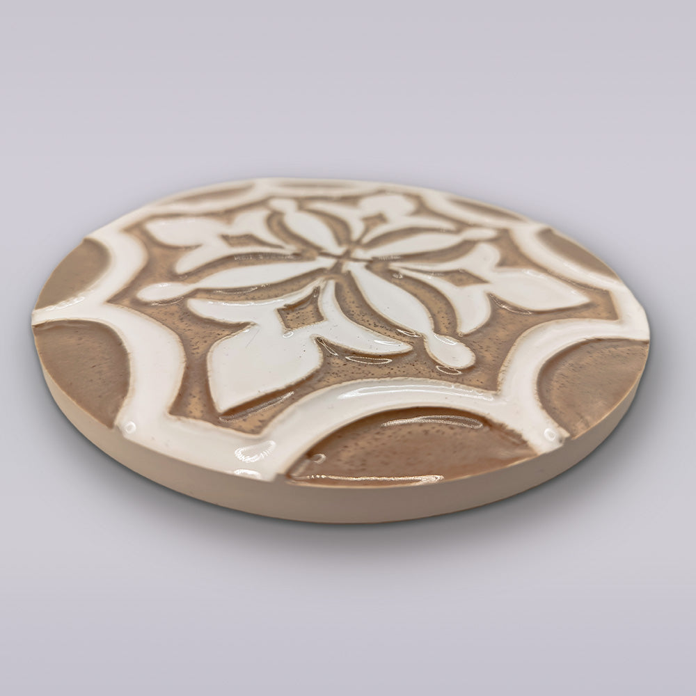The Ocre Fleur coaster by Miradouro Ceramics is a round Portuguese ceramic piece with a raised glossy white floral pattern on a light brown base—an elegant artisanal accent for any home.