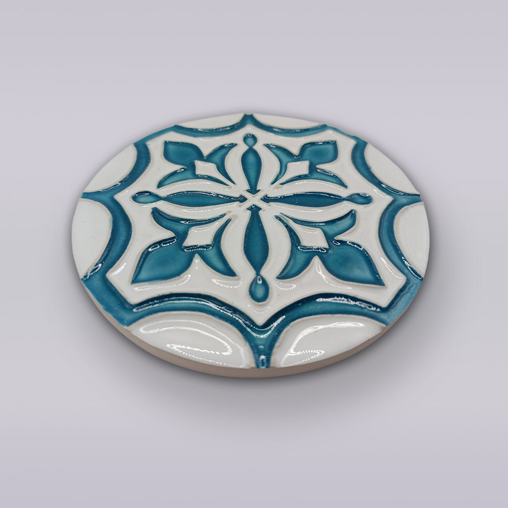 The Portuguese Flor-de-Lis Tile – Atlantic Edition by Miradouro Ceramics is a round ceramic coaster featuring an elegant blue and white floral-cross motif, reminiscent of classic tiles. A stylish accent for any space.