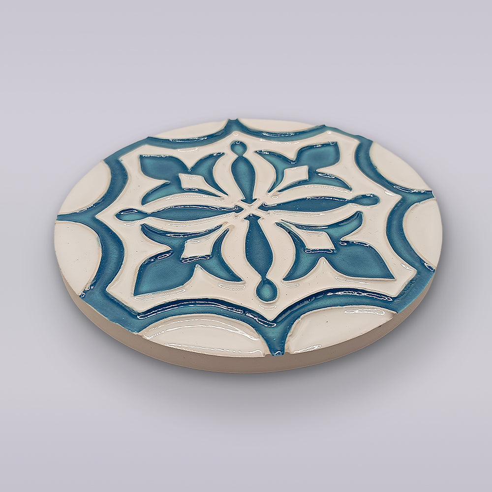 The Portuguese Flor-de-Lis Tile – Atlantic Edition by Miradouro Ceramics features a round ceramic design with a raised blue and white floral-cross motif, adding decorative flair to any space with its light gray background.
