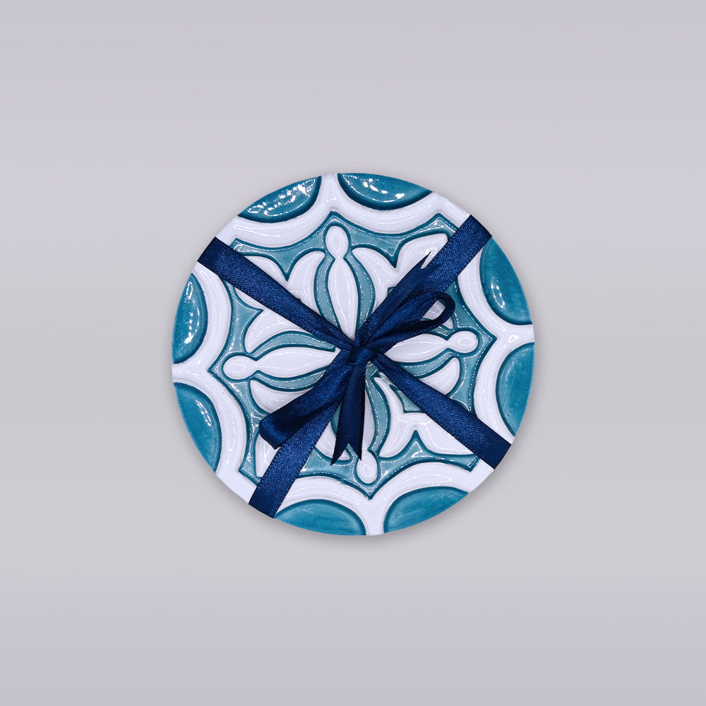 The Rosacrux Atlântica by Miradouro Ceramics is a round ceramic tile with a blue and white pattern, tied with a dark blue ribbon bow—a stylish accent displayed on a light gray background.
