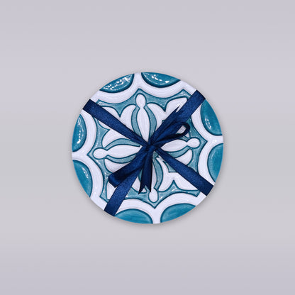 The Rosacrux Atlântica by Miradouro Ceramics is a round ceramic tile with a blue and white pattern, tied with a dark blue ribbon bow—a stylish accent displayed on a light gray background.