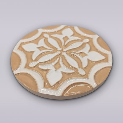 The Terra Manuelina by Miradouro Ceramics is a round, handcrafted ceramic coaster featuring a glossy beige and white geometric floral design inspired by Portuguese ceramics—an artisanal touch for your home decor.