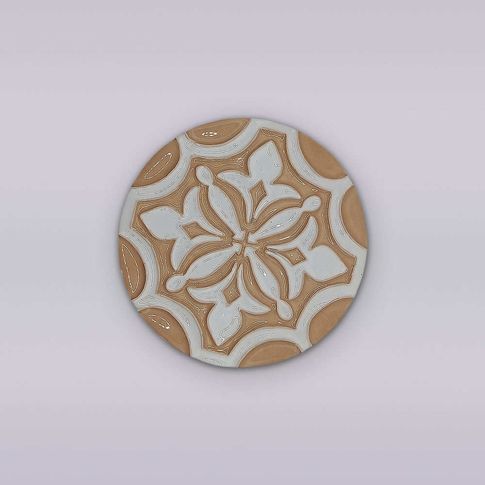 Add an elegant touch to your home with the Terra Manuelina round ceramic coaster by Miradouro Ceramics, featuring handcrafted floral and geometric patterns in beige and white on a light gray background.