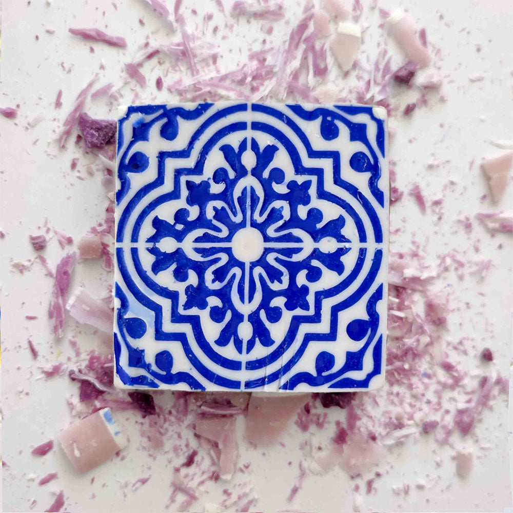 Lisbão's Violet Azulejo Ritual features a square tile with an intricate blue and white pattern, reminiscent of Portuguese design, surrounded by scattered pink and purple shards.
