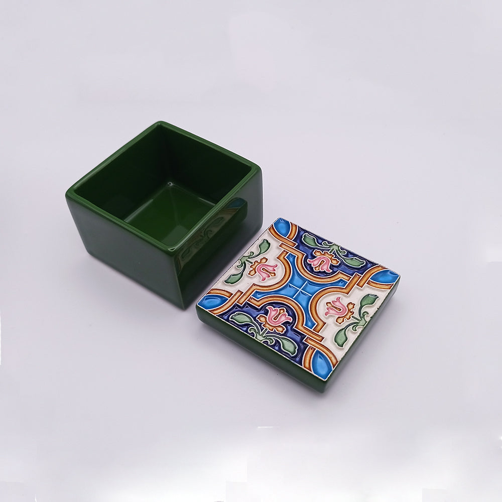 A small, square green Beja Ceramic Box by Tejo Shop with its lid removed and placed next to it. The lid features a colorful, intricate pattern with blue, red, green, and yellow designs on a white background. The box's interior and sides are solid green—a charming addition to your home decor that reflects rich heritage.