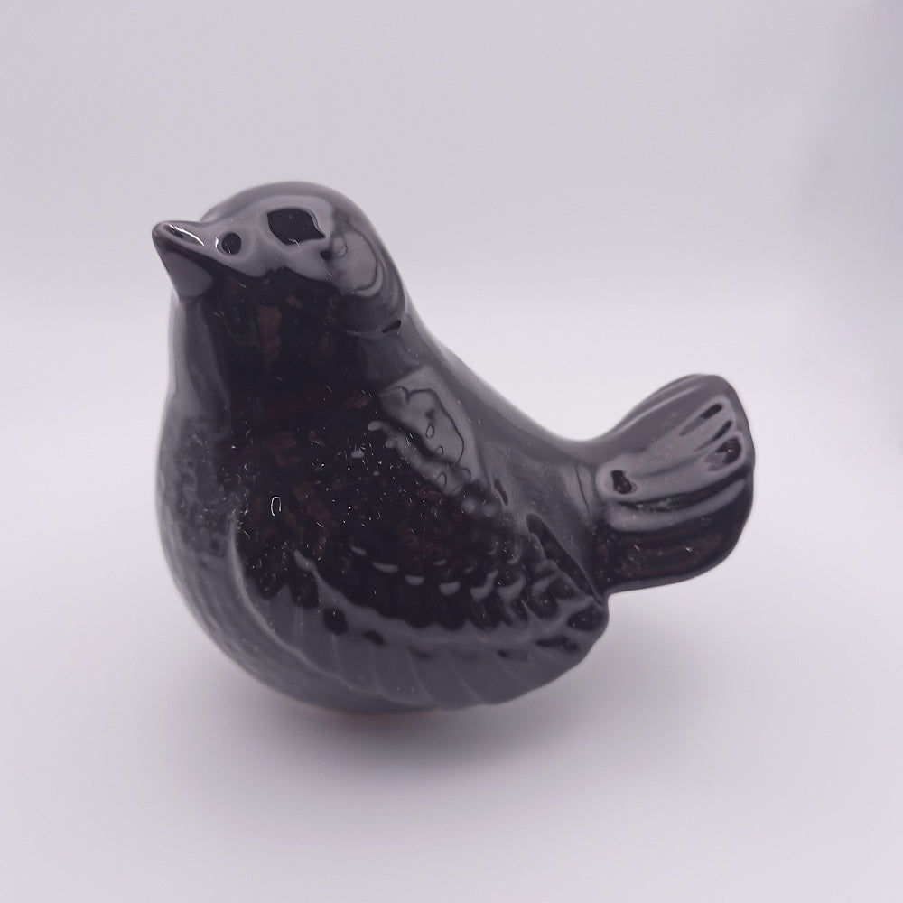 The Tejo Shop Ceramic Bird looking up Figurine is a small, handmade glossy black piece with a smooth texture, perched upright. It features simple, rounded characteristics and subtle details on its wings and body, exuding a minimalist yet elegant appearance. Perfect for home decor against a plain white background.