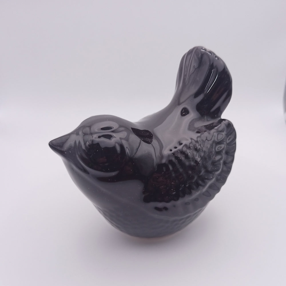 A small, handmade black Ceramic Bird Figurine from Tejo Shop stands against a plain white background. Featuring textured wings and tail, the bird has a glossy finish that gives it a sleek and polished appearance, making it perfect for home decor.