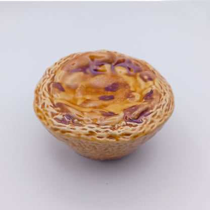 A close-up of a Ceramic Pastel de Nata from Tejo Shop showcases its golden, flaky crust and slightly browned top, perfectly highlighting its width against a plain white background.