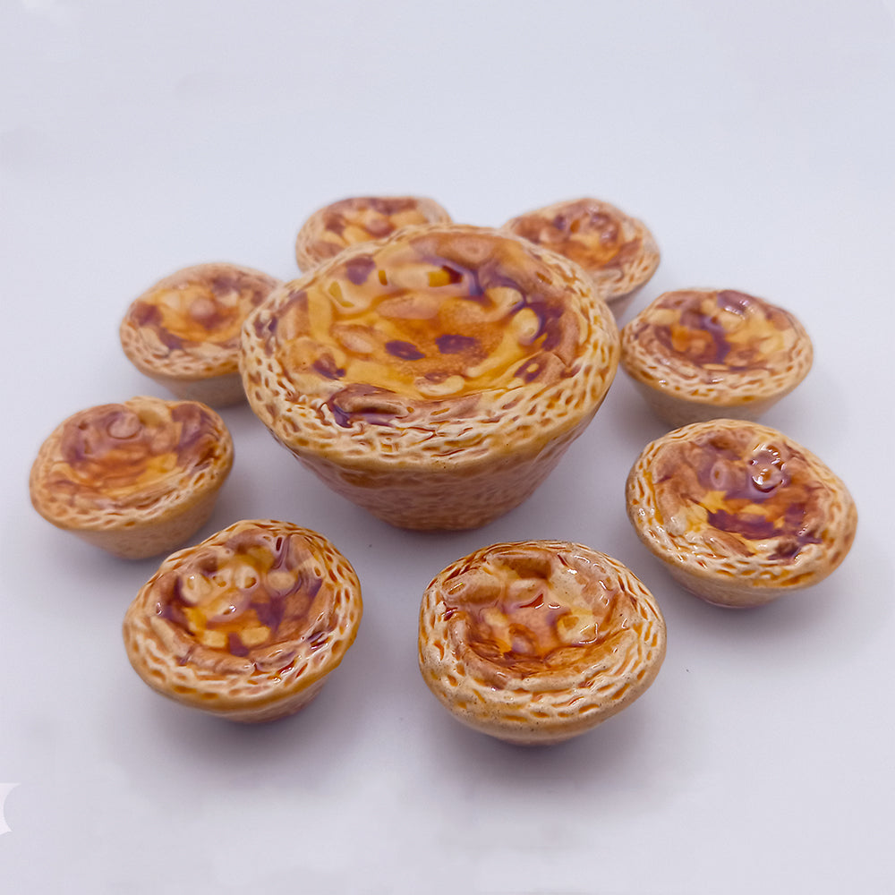 Eight miniature Ceramic Pastéis de Nata from Tejo Shop, each intricately detailed with a golden brown glaze, are elegantly arranged in a circle around a larger central tart. This charming setup is displayed against a plain white background, emphasizing the unique dimensions of each piece.