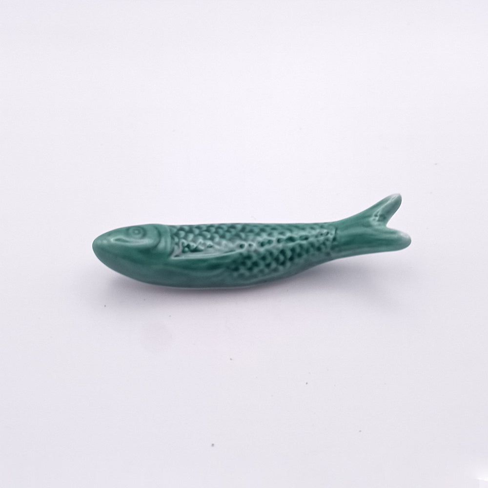 A Ceramic Sardine Fridge Magnet by Tejo Shop, shaped like a fish and glazed in a shade of green with a textured surface to mimic fish scales, reminiscent of a Portuguese icon, placed on a plain white background.