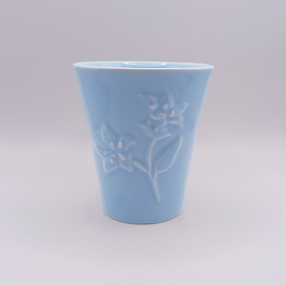 The Tejo Shop Ceramic Mug is a light blue ceramic cup with a minimalist design, featuring a delicate floral pattern embossed on one side against a plain background. Inspired by Portuguese art, this unique mug has a smooth, slightly flared shape with a glossy finish.