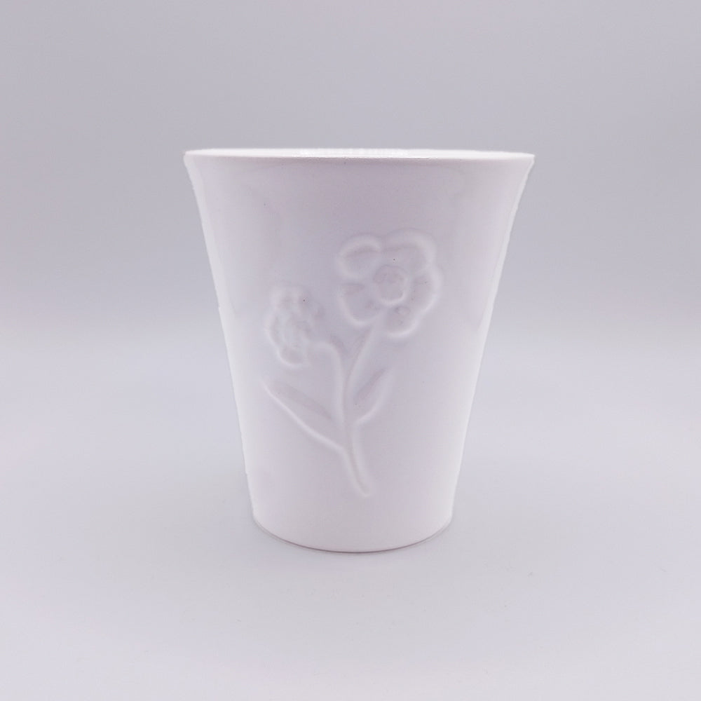 Introducing the Ceramic Mug by Tejo Shop: a stunning white ceramic cup with a smooth, glossy finish. This unique piece showcases a delicate embossed design of a blooming flower with leaves on the front. The plain light grey background enhances its simplicity and elegance, evoking the charm of Portuguese art traditions.