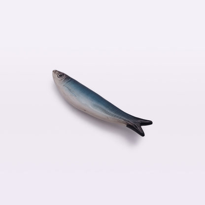 A realistic Ceramic Sardine Fridge Magnet from Tejo Shop with a blueish-gray gradient from top to bottom, resembling a lifelike sardine or similar small fish, is displayed against a plain white background. This hand-made piece, crafted in the tradition of Portuguese ceramics, is positioned horizontally.