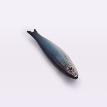 A realistic model of a fish, resembling a Ceramic Sardine Fridge Magnet from Tejo Shop, is shown on a plain white background. The fish has a slender, elongated body and features a gradient color scheme transitioning from dark blue on its back to white on its belly, with a prominent eye near its head.