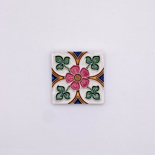 Decorative Mediterranean small ceramic tile featuring a floral design with a central pink flower surrounded by green leaves and geometric patterns in blue, orange, and white against a neutral backdrop from Tejo Shop.