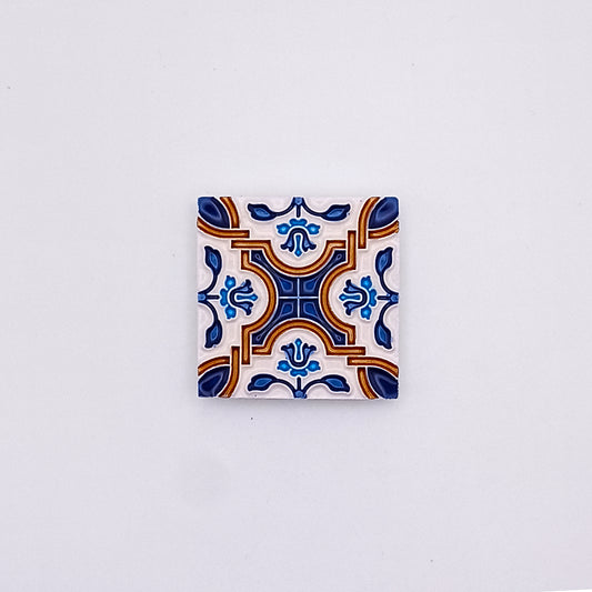 Decorative Mediterranean Hand Made Ceramic Tile with a symmetrical pattern in blue, orange, and white, centered on a plain, pale background from Tejo Shop.