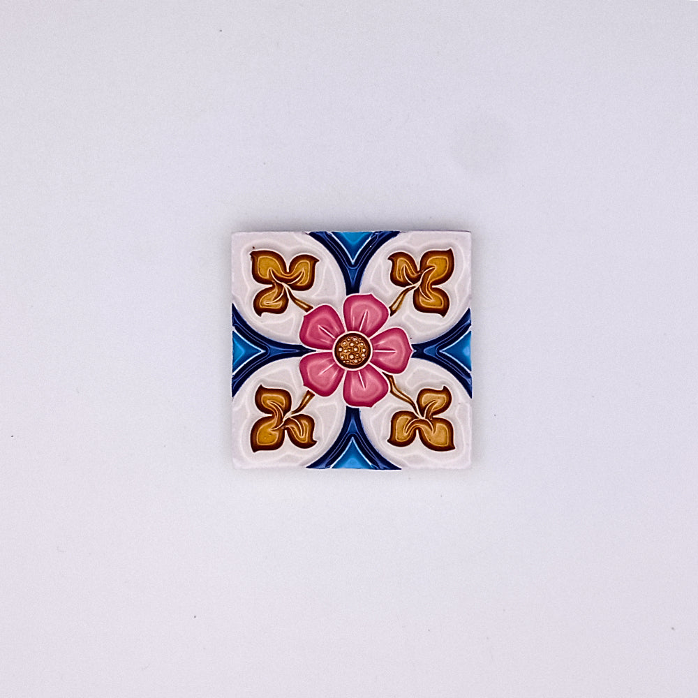 Square decorative hand-painted Tejo Shop small ceramic tile with a central pink flower design, surrounded by blue and gold patterns on a white background.